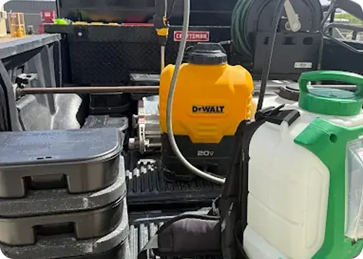 Truck bed loaded with DeWalt and FlowZone backpack sprayers and stacked bait stations.